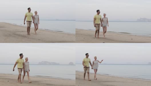 一对情侣在海滩上牵着手聊天，西班牙男人和年轻女人指指点点，游客度假高清在线视频素材下载