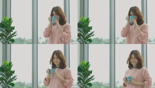 年轻美丽的亚洲女人喝咖啡，透过窗户与城市的看法与幸福，人们的生活方式高清在线视频素材下载
