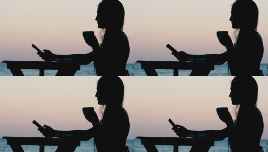 海边咖啡馆里的年轻女子。喝茶和使用智能手机高清在线视频素材下载