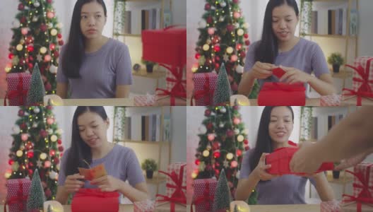亚洲妇女打开礼盒与笑脸在家里的背景与圣诞树装饰节日节日。圣诞节庆祝活动的概念。4 k慢动作。高清在线视频素材下载