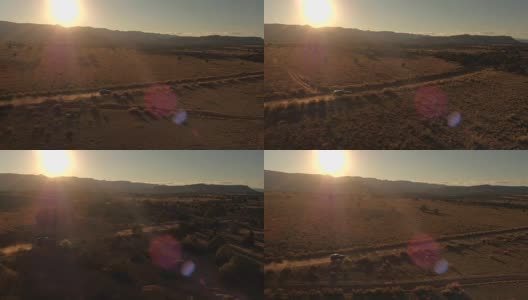 航拍:金色夕阳下，一辆黑色SUV行驶在沙漠山谷尘土飞扬的道路上高清在线视频素材下载