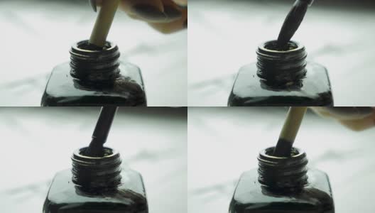 女人的手把毛笔浸在一罐近距离绘画的墨水里。中国传统的画笔选择焦点。中国画的细节，同时在光线的背面画一条线高清在线视频素材下载