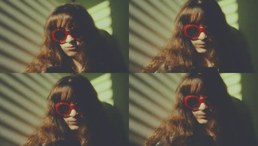 透过百叶窗的光线，映入眼帘的是一个戴着红色太阳镜的穿孔女孩，她正在用智能手机冲浪。慢动作拍摄高清在线视频素材下载