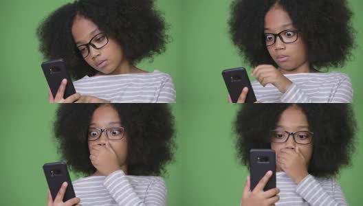 年轻可爱的非洲女孩与非洲发式看起来震惊，而使用电话高清在线视频素材下载