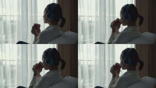 亚洲妇女放松听音乐与她的杯子靠近窗户的场景高清在线视频素材下载