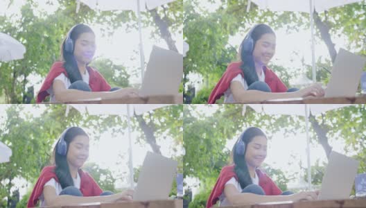亚洲美丽的少女戴着耳机使用笔记本电脑坐在花园里学习在线。视频网络研讨会。在家远程视频会议。业务网上购物。在家里工作。网上注册高清在线视频素材下载