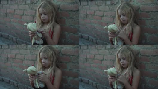 一个来自贫困家庭的蓬头垢面的小女孩在一堵砖墙前玩着她的玩具。高清在线视频素材下载
