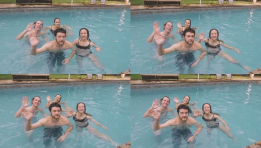 两名年轻女子和两名男子挥手告别，看着镜头在游泳池里游泳高清在线视频素材下载