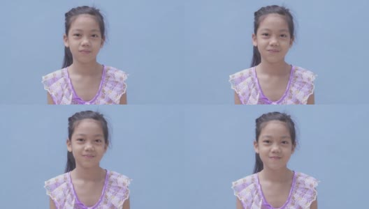 微笑自信的亚洲小女孩脸上的微笑，亚洲孩子站在蓝色的背景。一个看着相机的孩子的肖像高清在线视频素材下载