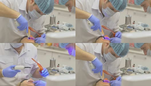 牙医在一间现代化的牙科诊所里为病人治疗。牙齿矫正医师有一个助手。病人用蓝色激光牙消毒。橙色的玻璃百叶窗用于保护眼睛。高清在线视频素材下载
