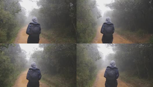 徒步女子背包行走在热带潮湿的森林。年轻的女孩在旅行中穿着雨衣在森林小径上。跟随女游客踩在丛林小径。慢镜头后视图高清在线视频素材下载