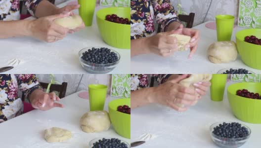 一位妇女用手揉面包饺子。桌子上的下一道菜是蓝莓和樱桃做馅。高清在线视频素材下载