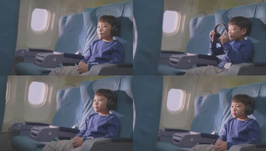 亚洲小男孩在飞机上触摸屏幕，然后看电影和卡通。孩子们感到高兴和兴奋的飞机旅行和享受机上娱乐。高清在线视频素材下载