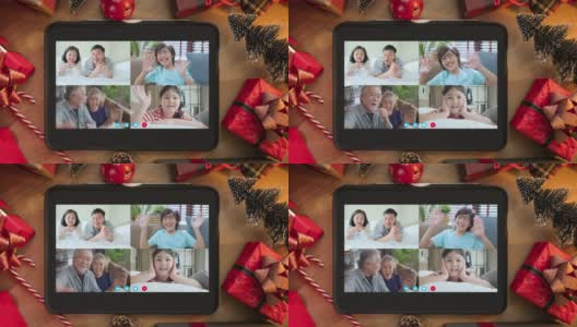 视频蒙太奇的亚洲家庭关系连接人们挥手和幸福微笑一起看着平板电脑放在木地板上的圣诞节装饰项目Voip概念高清在线视频素材下载