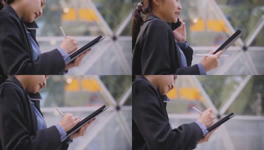 亚洲女商人使用笔记本电脑，在城市的办公室前用她的手机交谈高清在线视频素材下载