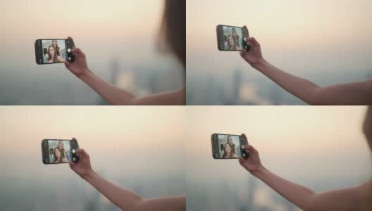 日落时分，4K的亚洲女性朋友在摩天大楼的屋顶餐厅一起用智能手机自拍。高清在线视频素材下载