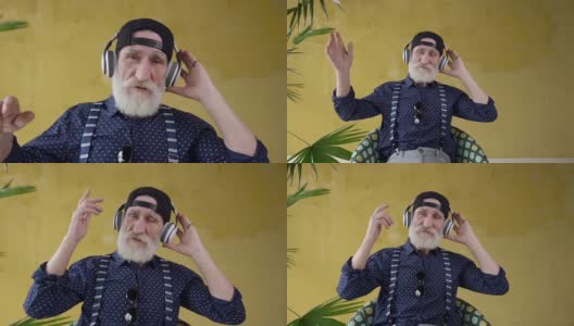 英俊潇洒的留着胡子的70岁男子戴着耳机听着美妙的音乐，看着相机高清在线视频素材下载