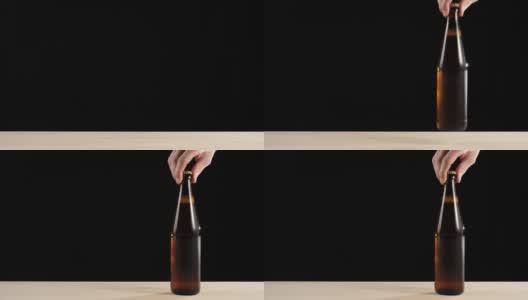 新鲜的啤酒。Hand把一个棕色的瓶子和美味的精酿啤酒放在一张黑色背景的木桌上。冰镇新鲜啤酒与水滴。准备饮料。广角镜头。4 k高清在线视频素材下载