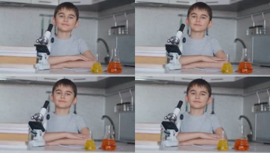 一个聪明的学生坐在家里的桌子旁边，旁边是一个显微镜和装有液体的瓶子高清在线视频素材下载