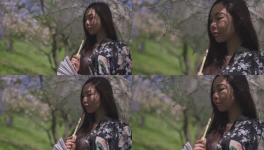 年轻的亚洲美女手持白色太阳伞，在阳光明媚的春日里在公园里思考。迷人艳丽的日本女士在户外享受大自然的侧视图肖像。缓慢的运动。高清在线视频素材下载