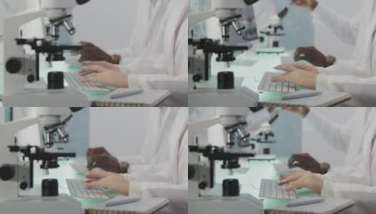 非洲和亚洲的科学家正在研究DNA样本。电脑屏幕和显微镜。近距离做笔记高清在线视频素材下载