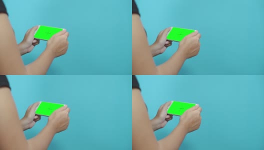一名女性在蓝色桌面上使用绿色屏幕的智能手机。女性的手滚动页面，轻触触摸屏。高清在线视频素材下载