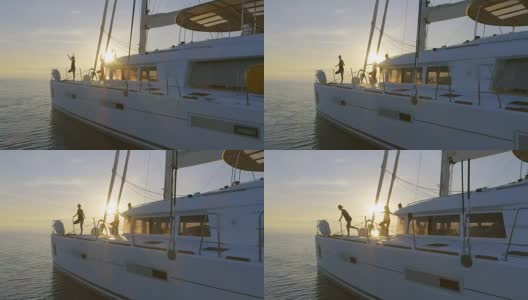 航拍三个美丽的健康妇女在一艘白色帆船上做晨瑜伽。平静的大海与升起的太阳和平静的大海。高清在线视频素材下载
