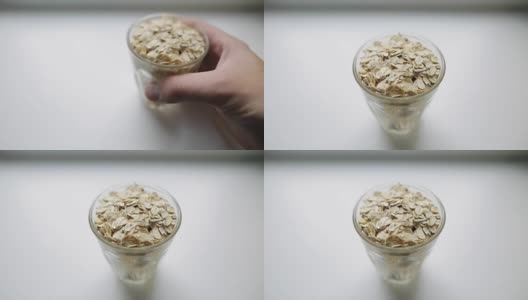 健康的早餐，燕麦粥。一个白种人的手把透明的玻璃和大燕麦片放在白色的表面。有机早餐，强健肌肉。高清在线视频素材下载