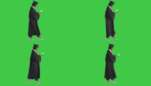 年轻的美国黑人女学生穿着黑色毕业礼服，拿着文凭，在绿色屏幕上使用手机，Chroma Key高清在线视频素材下载