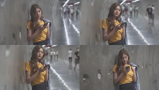 年轻美丽的亚洲女子在地铁站用智能手机上网和手机应用的高清慢镜头。迷人的女孩拿着手机，发着在线短信。科技与城市生活理念。高清在线视频素材下载