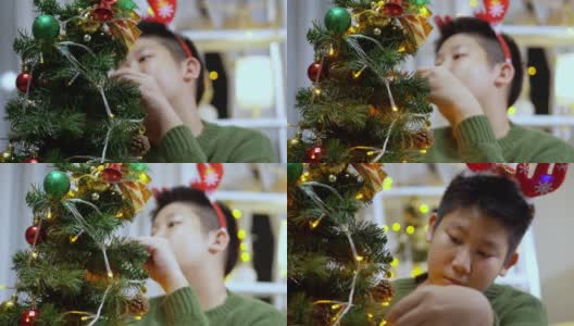 快乐的亚洲男孩穿着绿色的毛衣和红色的发带装饰圣诞树在晚上的时间在家里，节日的概念。高清在线视频素材下载