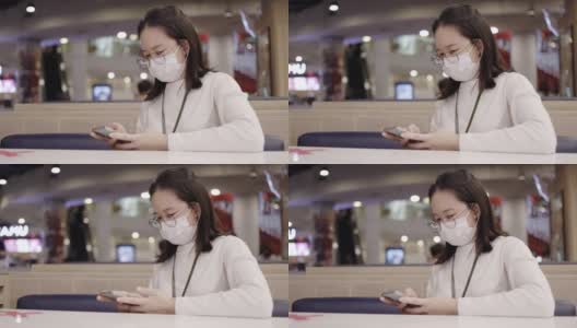 亚洲商界女性戴口罩预防冠状病毒感染。使用智能手机了解COVID-19疫情。在社区或餐厅保持社交距离。医疗保健新常态高清在线视频素材下载