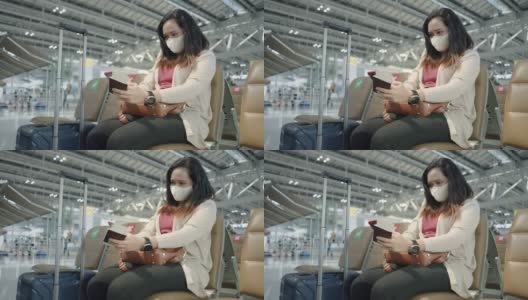 侧面低视角:只有亚洲女性穿着粉色t恤，戴着防护COVID-19的口罩，带着行李、护照、机票，在机场等待新的旅程、旅行、度假时使用智能手机、触摸社交媒体。高清在线视频素材下载