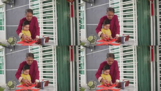 亚洲华人微笑的爷爷和孙子在中国新年期间在前院手写中国书法高清在线视频素材下载