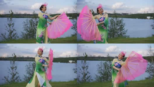 美丽的中国女孩穿着中国传统服装，拿着大粉扇在河岸上跳舞高清在线视频素材下载