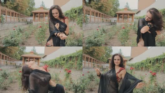 性感的女人在黑色面纱的东方舞蹈与玫瑰在花园里美丽的舞蹈慢动作高清在线视频素材下载