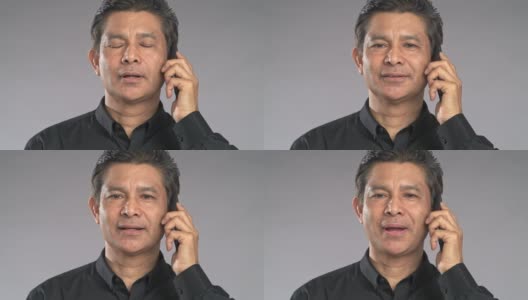 近景老人正在打手机，面无表情，孤立在灰色背景中。穿着黑衬衫的亚洲人。高清在线视频素材下载