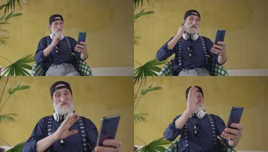 前面的有趣的快乐有吸引力的大胡子老男人有视频聊天电话，坐在椅子上的黄色背景高清在线视频素材下载