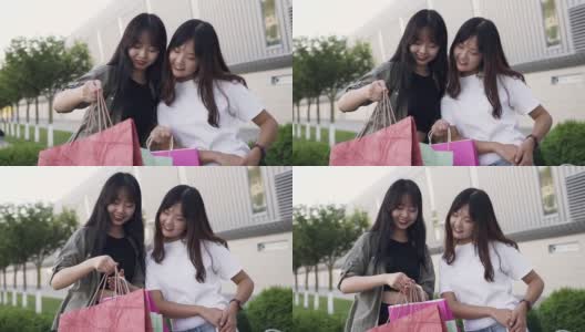 两个迷人的无忧无虑的亚洲女性最好的朋友站在购物中心的墙壁和展示什么是在购物后的纸袋高清在线视频素材下载
