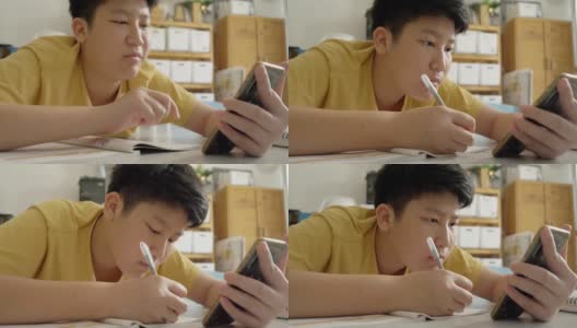 亚洲男孩躺在地板上做作业，同时在家学习在线课程，社交距离的生活方式概念。高清在线视频素材下载