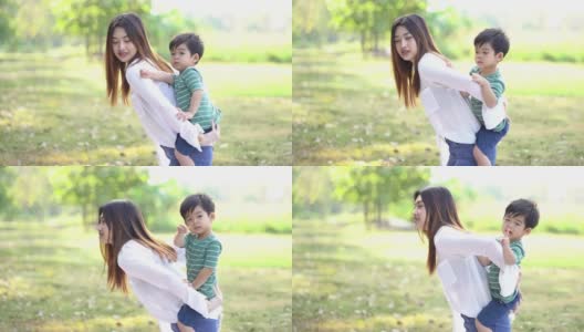 年轻的亚洲母亲背着可爱的小男孩在公园里玩耍。妈妈让婴儿背在背上。幸福的家庭和友谊的概念。高清在线视频素材下载