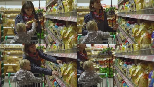 一位带着孩子的年轻妇女在超市选购商品。妈妈正用手推车载着一个小女孩。妈妈和女儿选择食物。高清在线视频素材下载
