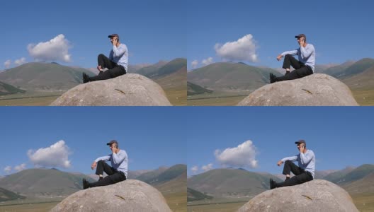 男人坐在山上的大石头上用手机打电话高清在线视频素材下载
