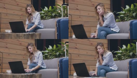 一个30岁金发美女坐在酒店大堂的软沙发上用笔记本电脑打字的慢镜头高清在线视频素材下载