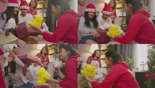 亚洲少女惊喜礼物盒给她可爱的哥哥和妹妹，而庆祝她的家人在圣诞节假期在家里的客厅。两个兄弟拥抱和微笑。高清在线视频素材下载