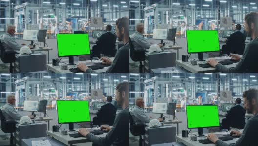 汽车工厂办公室:白人男性汽车工程师坐在他的办公桌上工作的绿色屏幕色度键电脑。自动化机械臂装配线制造。过肩中拍高清在线视频素材下载