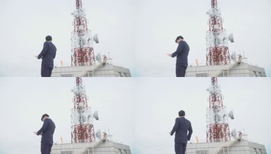 身穿西装、手持平板电脑站在电信塔屋顶的快乐亚洲商人高清在线视频素材下载