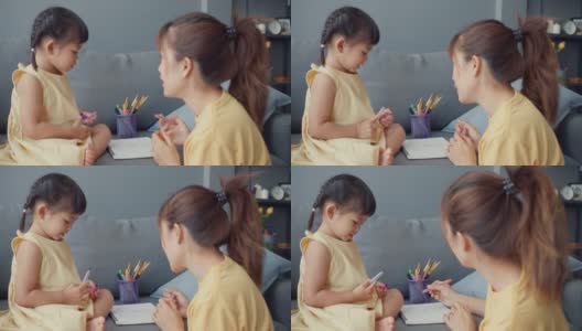 快乐快乐的亚洲家庭妈妈教女孩画画，使用相册和彩色铅笔在家里客厅的沙发上放松。高清在线视频素材下载