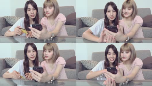 快乐的年轻亚洲女性与朋友持有信用卡和使用智能手机在家里网上购物高清在线视频素材下载