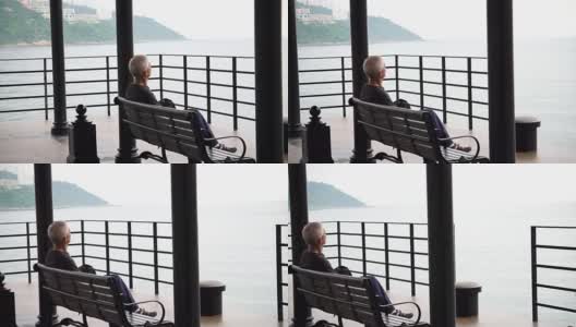 在阴沉的雨天，亚洲老人独自站在海滩前的码头上高清在线视频素材下载
